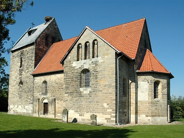 Sigwardskirche Romanische Kirche aus Naturstein mit rotem Ziegeldach, umgeben von Grünfläche und Bäumen.