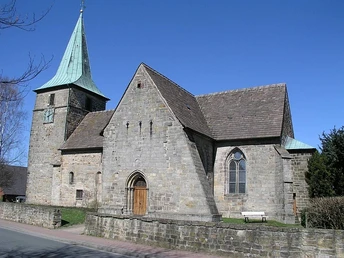 Bergkirchen Historische Steinkirche mit markantem Turm und Spitzdach, umgeben von blauem Himmel und Bäumen.