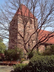 Buchholz Eine historische Backsteinkirche mit roten Dachziegeln, umgeben von Bäumen ohne Laub.