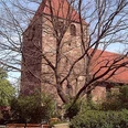 Buchholz Eine historische Backsteinkirche mit roten Dachziegeln, umgeben von Bäumen ohne Laub.