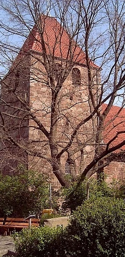 Buchholz Eine historische Backsteinkirche mit roten Dachziegeln, umgeben von Bäumen ohne Laub.