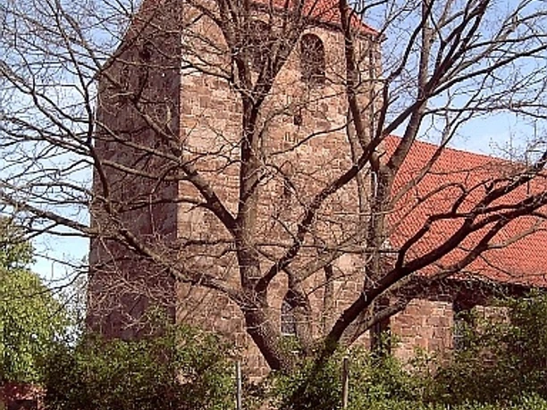 Buchholz Eine historische Backsteinkirche mit roten Dachziegeln, umgeben von Bäumen ohne Laub.