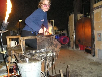 Glashütte Gernheim Eine Glasmacherin kreiert mit traditionellen Methoden ein leuchtend blaues Glas im Ofenraum.