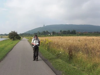 Wanderweg an der Weser Ein Wanderer läuft auf einem asphaltierten Weg entlang der Weser, umgeben von Feldern und Bäumen.