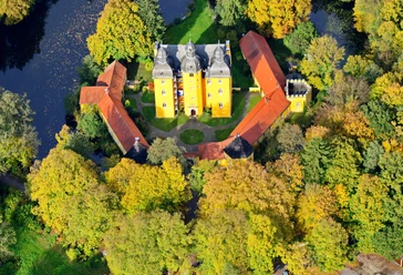 Holter Jagdschloss Luftbild Luftaufnahme des gelben Holter Jagdschlosses mit drei Gebäudeflügeln, umgeben von Herbstbäumen.