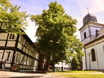 Bebauung am Kirchring Fachwerkhaus mit Baum und Kirche im sonnigen Dorfplatz, umgeben von historischem Charme.