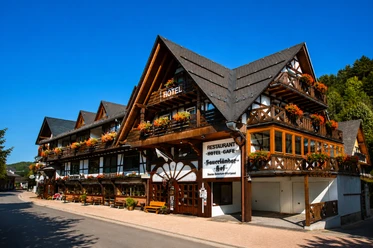 Hausansicht Hotel Sauerländer Hof Willingen Hotel Sauerländer Hof in Fachwerkoptik mit Balkonen, Blumenschmuck, Restaurant-Schild und blauem Himmel in Willingen