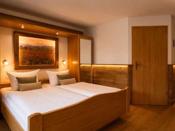 Doppelzimmer Bettansicht Hotel Sauerländer Hof Willingen Doppelzimmer im Hotel Sauerländer Hof mit Holzbett, weißen Decken, Kissen, warmem Licht und Wandbild über dem Bett.