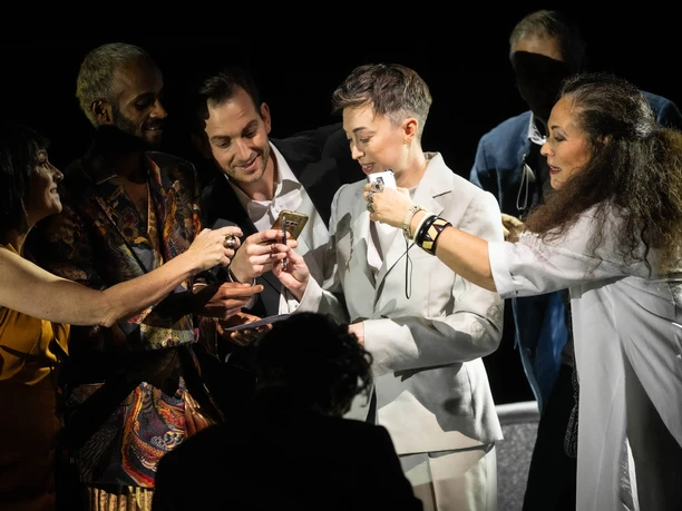 Extras from the Cologne Opera, Bianca Andrew, KS Dalia Schaechter Opera scene from *Der Rosenkavalier*: The ensemble surrounds a person in a white suit holding cell phones