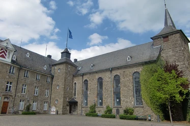 Schloss Hückeswagen Historisches Schloss mit steinernen Fassaden, Türmen und großen Fenstern im Innenhof bei blauem Himmel.