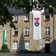 Schloss Hückeswagen Ein historisches Steingebäude mit Blumenkästen, Fahnen und einem gepflasterten Hof im Vordergrund.