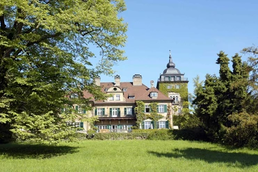 Schloss Lerbach Historisches Schloss mit Türmchen und grüner Fassade, umgeben von malerischen Bäumen und Wiesen.