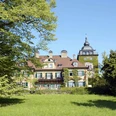 Schloss Lerbach Historisches Schloss mit Türmchen und grüner Fassade, umgeben von malerischen Bäumen und Wiesen.