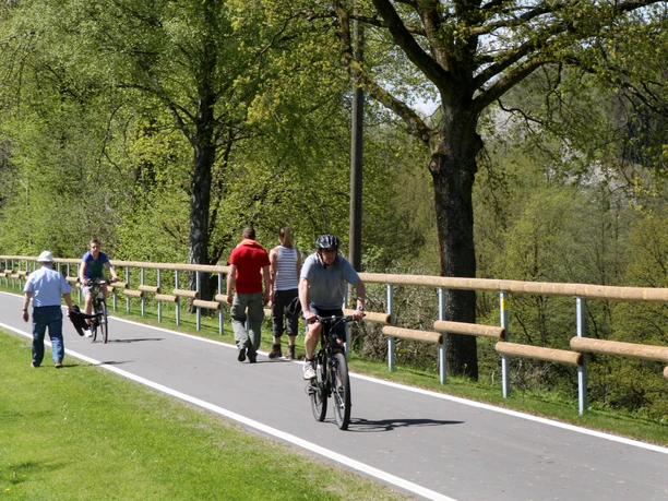 Bahntrasse Sülztalbahn Menschen fahren Rad und spazieren auf einem von Bäumen gesäumten, sonnigen Radweg im Grünen.