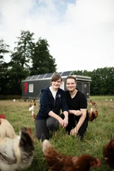 Delbrück_Noltenhof.jpg Two people are sitting on the lawn among the chickens and smiling at the camera