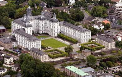 Blick auf Schloss Bensberg Luftaufnahme des barocken Schloss Bensberg in Bergisch Gladbach, umgeben von Grünflächen und Bäumen.