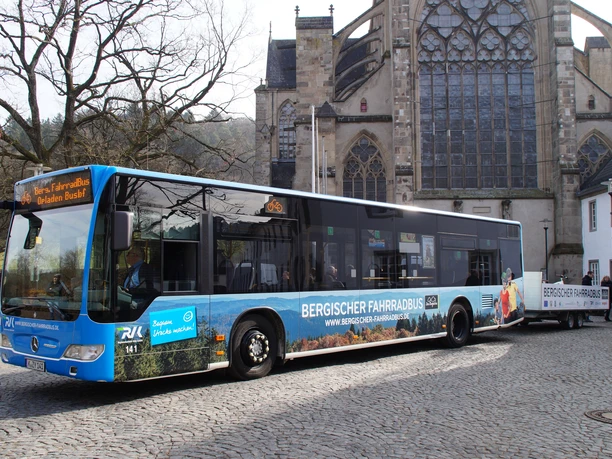 Bergischer FahrradBus Ein moderner Fahrradbus vor einer historischen Kirche auf einem gepflasterten Platz in Odenthal.