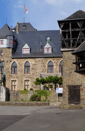 Mittelalterliche Burg mit Zinnen und Türmen, Steinwände, Statue im Innenhof, blauer Himmel.