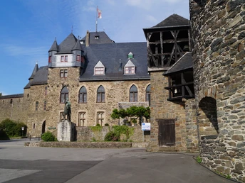 Schloss Burg Mittelalterliche Burg mit Zinnen und Türmen, Steinwände, Statue im Innenhof, blauer Himmel.