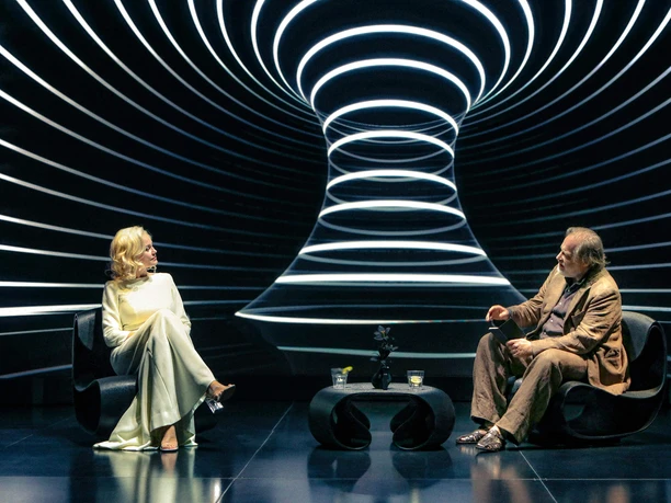 Moneyland - Bettina Lieder, Benjamin Höppner Zwei Schauspieler auf futuristischer Bühne mit leuchtenden Kreislinien im Hintergrund