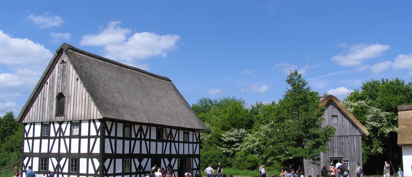 LVR-Freilichtmuseum Lindlar Zwei traditionelle Fachwerkhäuser mit Reetdächern und viele Besucher an einem sonnigen Tag im Freilichtmuseum.