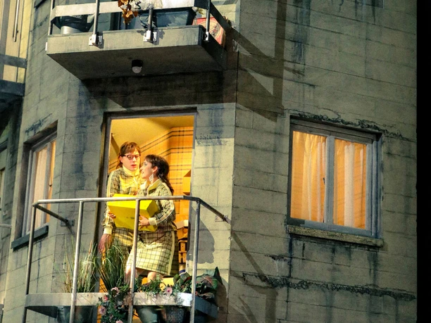 In bester Lage - Jonas Dumke, Rebekka Biener, Fabian Reichenbach A theater scene from “In Bester Lage” featuring people at the windows and on the balconies of a building’s facade