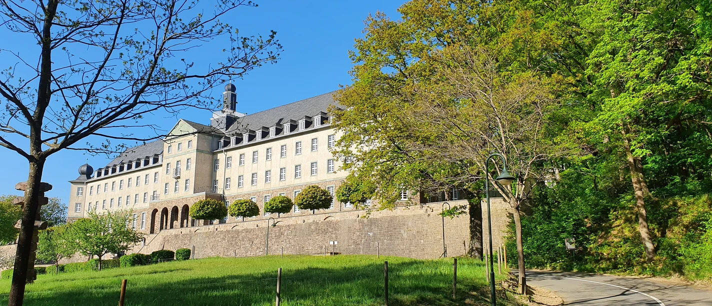 Kardinal Schulte Haus Zufahrtsstraße zum Kardinal-Schulte-Haus mit Wiese, Bäumen und blauem Himmel