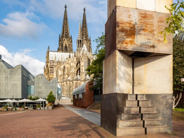 MA'ALOT Kölner Dom hinter moderner Skulptur auf einem gepflasterten Platz der Altstadt