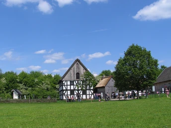 LVR-Freilichtmuseum Lindlar Fachwerkhaus in einem grünen Landschaftspark, Bäume im Hintergrund, blauer Himmel mit wenigen Wolken.