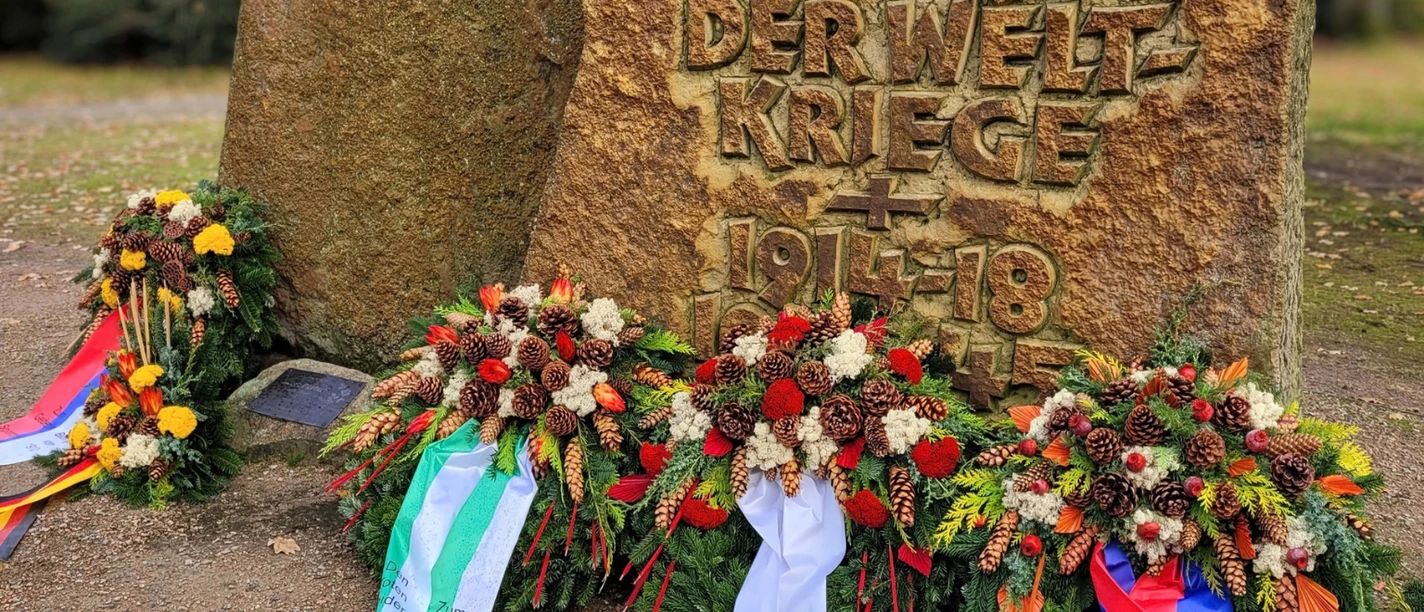 Volkstrauertag .png Gedenkstein für die Opfer der Weltkriege mit Kränzen und Schleifen in Bispingen.