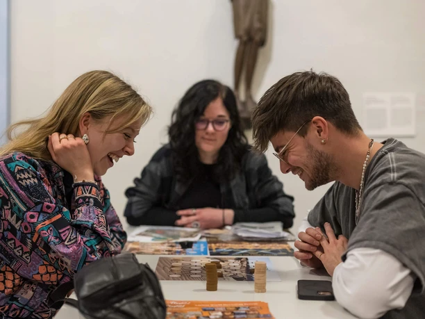 Boardgame Night im Museum Schnütgen Drei junge Erwachsene spielen lachend ein Brettspiel im Museum Schnütgen in Köln.