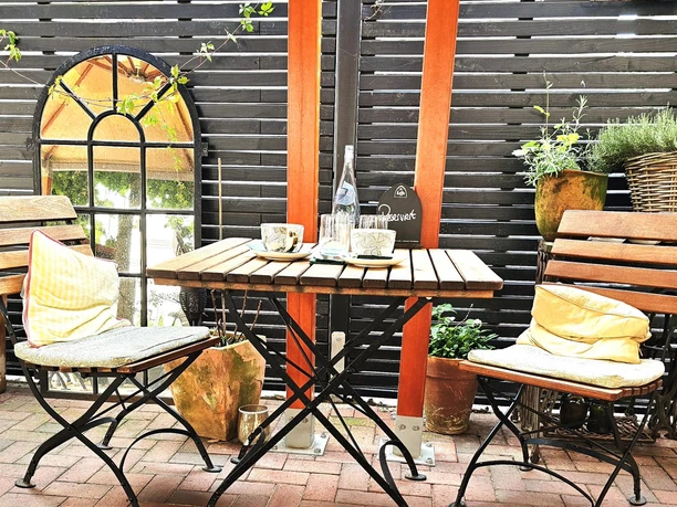 Bistro Lugenstein Terrassentisch mit zwei Stühlen, Kaffeetassen, Wasserflasche und Topfpflanzen.
