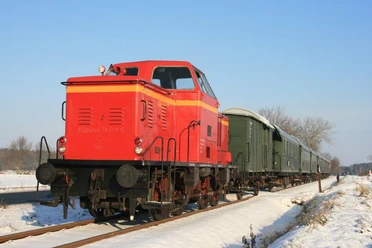 winterfahrt-ccbysa-foto©heide-express.jpg Rote Lok des Heide-Express mit grünen Waggons auf verschneiter Strecke.