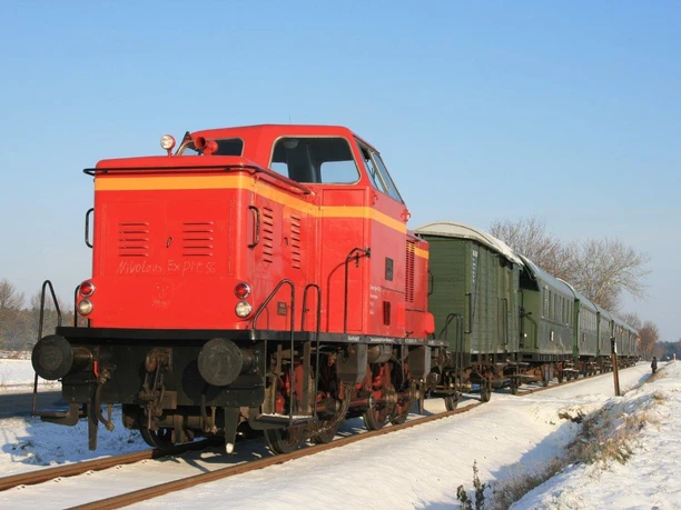 winterfahrt-ccbysa-foto©heide-express.jpg Rote Lok des Heide-Express mit grünen Waggons auf verschneiter Strecke.