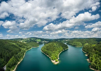 Aggertalsperre Panoramablick auf einen von Wäldern umgebenen, blaugrünen See unter einem bewölkten Himmel.
