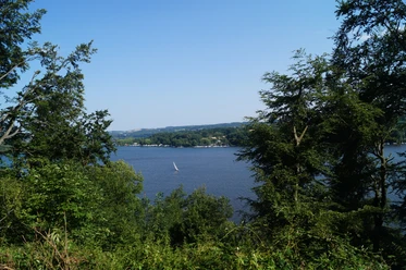 Blick auf den Baldeneysee <p>Blick durch Bäume auf den Baldeneysee in Essen mit Segelboot bei klarem Himmel.</p>