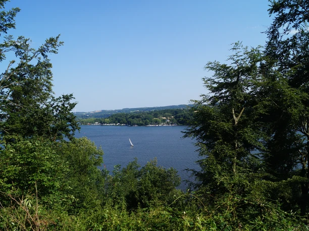 Blick auf den Baldeneysee <p>Blick durch Bäume auf den Baldeneysee in Essen mit Segelboot bei klarem Himmel.</p>