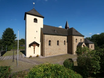 Kirche St. Johann Baptist in Kreuzkapelle Romanische Kirche mit hellem Turm und Kreuz, umgeben von grünem Laub und klarem, blauem Himmel.