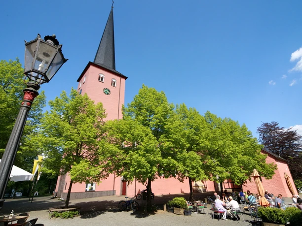 St. Martinus Kirche in Much <p>Historische Kirche in Much: rote Fassade, hoher Turm, sommerlicher blauer Himmel, grüne Bäume.</p>