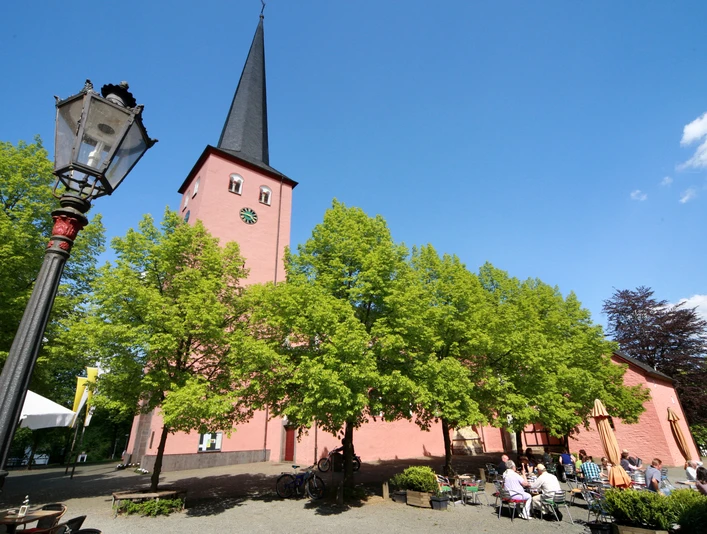 St. Martinus Kirche in Much <p>Historische Kirche in Much: rote Fassade, hoher Turm, sommerlicher blauer Himmel, grüne Bäume.</p>
