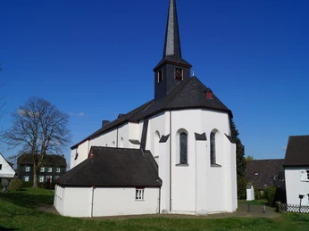 St. Katharina in Stadt Blankenberg <p>Eine weiße Dorfkirche mit schwarzem Turm und umgebenden Gebäuden vor blauem Himmel.</p>
