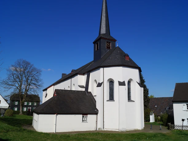 St. Katharina in Stadt Blankenberg <p>Eine weiße Dorfkirche mit schwarzem Turm und umgebenden Gebäuden vor blauem Himmel.</p>