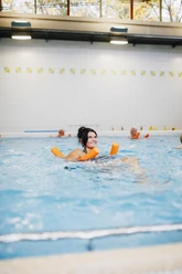 Eine Frau mit einem Schwimmhilfe im Wasser lächelt. Im Hintergrund sind weitere Schwimmer zu sehen.