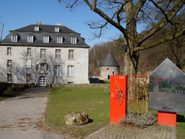 Schloss Hardenberg Historisches, steinernes Herrenhaus mit Infotafel im Vordergrund; bewaldete Umgebung im Hintergrund.