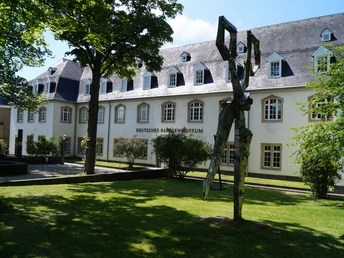 Deutsches Klingenmuseum Historisches Gebäude mit weißen Fensterrahmen, Skulptur im Vordergrund, umgeben von Bäumen.