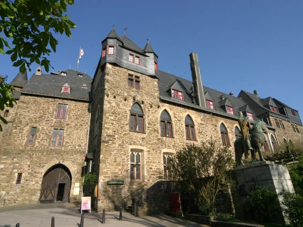 Schloss Burg Burg mit historischem Mauerwerk und Statue von Ritter auf Pferd im Vordergrund, blauer Himmel darüber.