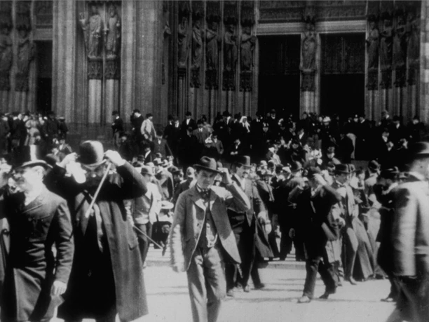 “At Cologne Cathedral After the Main Service” / “Sortie de la cathédrale” A crowd in front of Cologne Cathedral in a historic black-and-white photograph from 1896