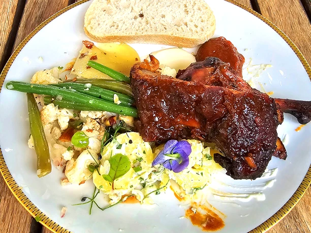 Bistro Lugenstein BBQ-Abend BBQ-Teller mit glasierten Rippchen, Brot, Bohnen und Kartoffelsalat auf Holztisch. Eine Reservierung wird empfohlen.