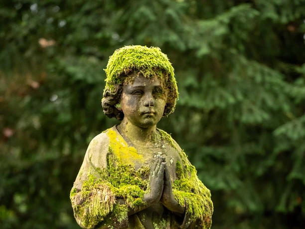Melaten Cemetery in Cologne A moss-covered statue of a child with folded hands at the Melaten Cemetery
