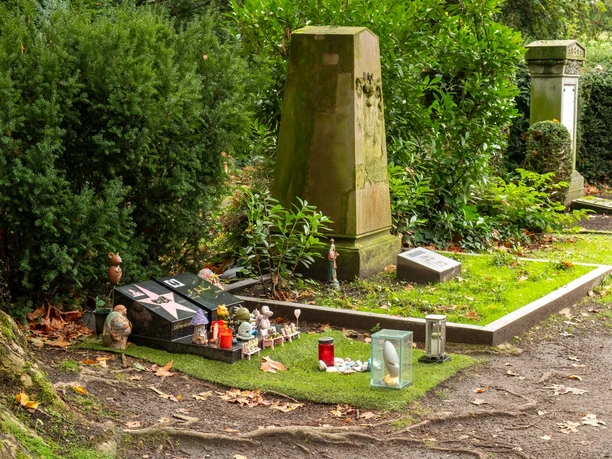 Melaten-Friedhof in Köln Grabstätte des Schauspielers und Komikers Dirk Bach auf dem Melaten-Friedhof in Köln, geschmückt mit Kerzen, Figuren und persönlichen Erinnerungsstücken.